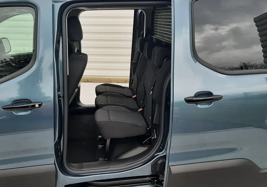 Vue latérale gauche du Peugeot Rifter bleu Kiama avec porte coulissante ouverte révélant les trois sièges individuels arrière.