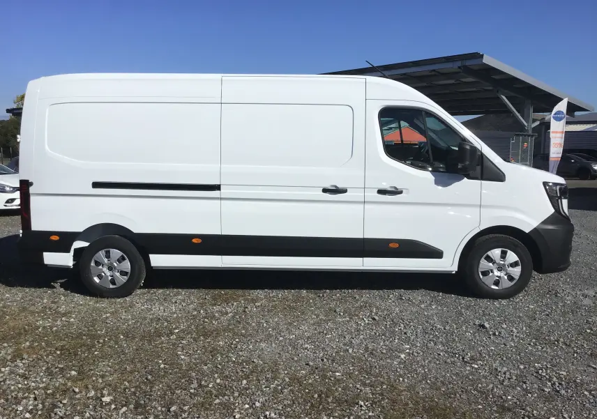 Profil droit d'un utilitaire blanc Renault Master L3H2 2025 avec bande noire et jantes argentées sur sol gravillonné.