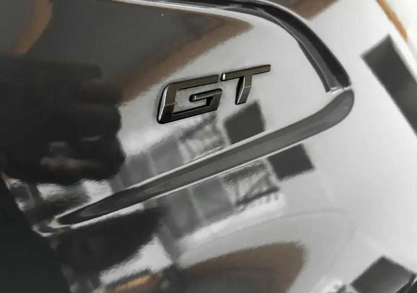 Gros plan sur l'emblème GT noir brillant sur la carrosserie gris foncé d'une Peugeot 208 Hybrid 136 eDCS6 GT.