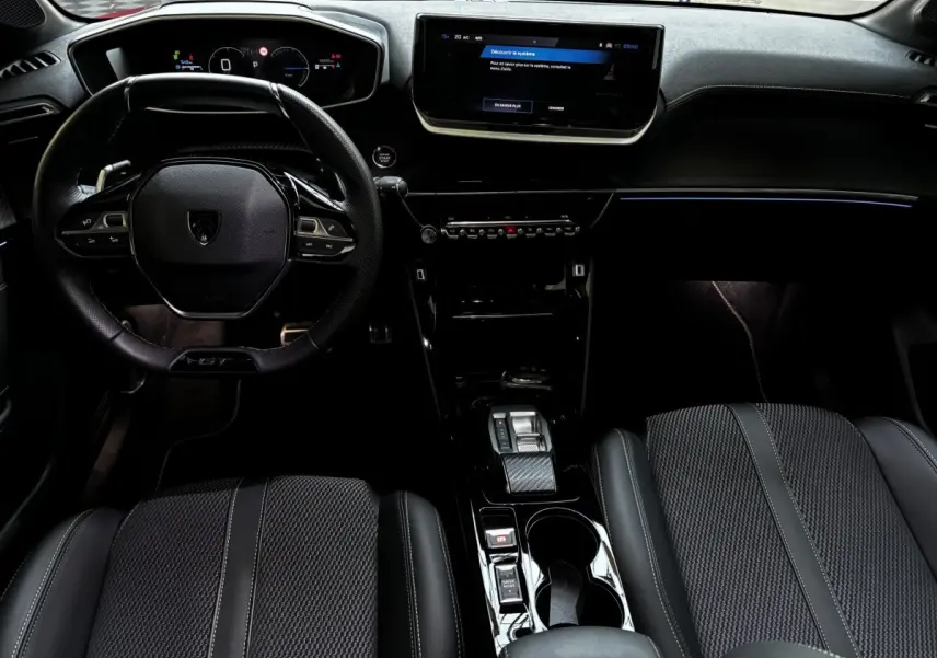 Intérieur Peugeot 208 Hybrid 136 GT vu de face, volant cuir, écran tactile central et sièges noirs texturés.