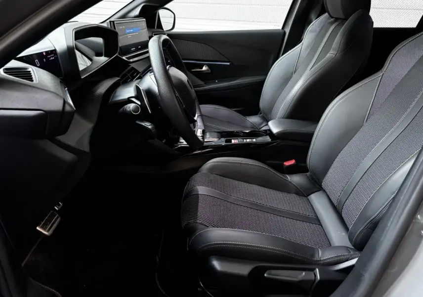 Intérieur avant droit de la Peugeot 208 Hybrid 136 eDCS6 GT 2024 avec sièges gris et tableau de bord numérique.