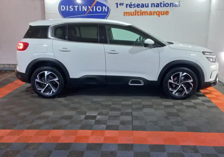 Profil droit d'un SUV Citroën C5 Aircross blanc avec jantes alliage et protections noires basses, en intérieur showroom.