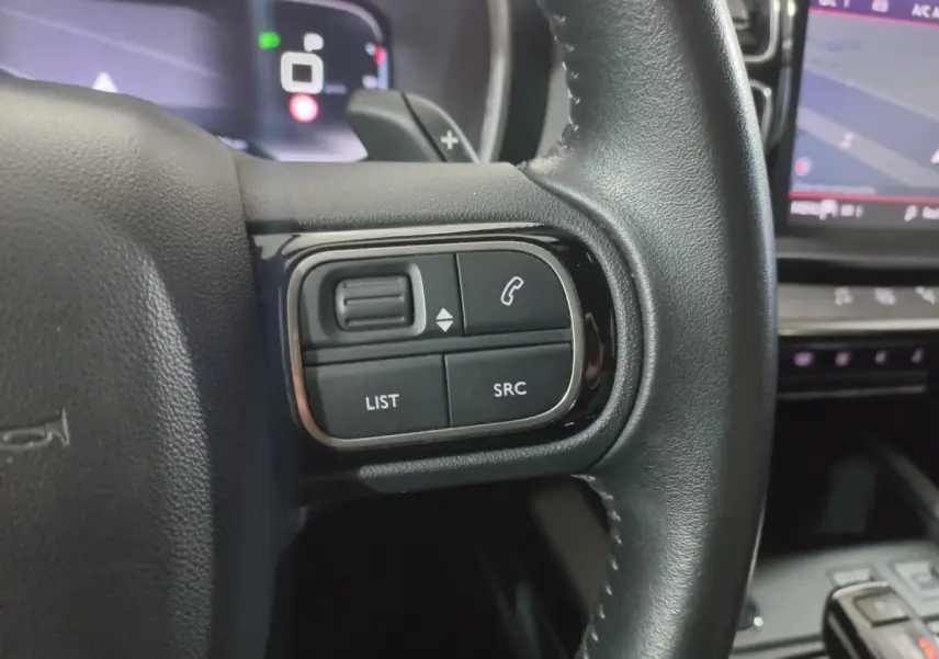 Gros plan sur les commandes gauche du volant cuir noir du Citroën C5 Aircross 2020 avec écran tactile en arrière-plan.