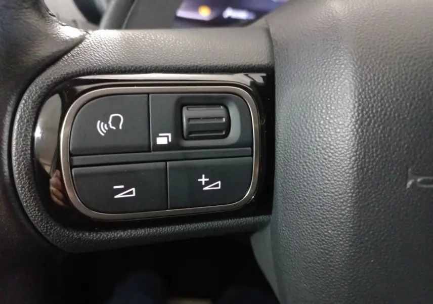 Gros plan sur les commandes vocales et volume sur le côté gauche du volant cuir du Citroën C5 Aircross blanc.