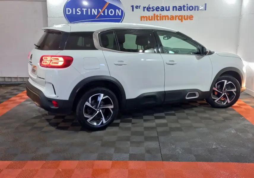Vue de profil côté gauche d'un Citroën C5 Aircross blanc avec feux arrière allumés en intérieur showroom.