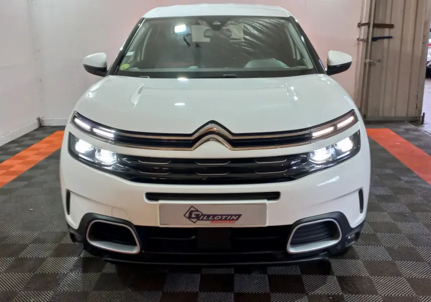 Vue de face d'un Citroën C5 Aircross blanc avec phares allumés et calandre distinctive dans un garage.