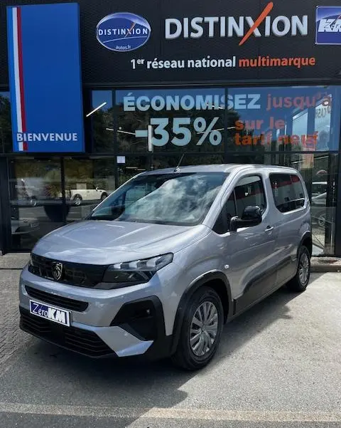 Peugeot Rifter gris foncé vue 3/4 avant droit devant un showroom Distinxion avec logo et vitres réfléchissantes.