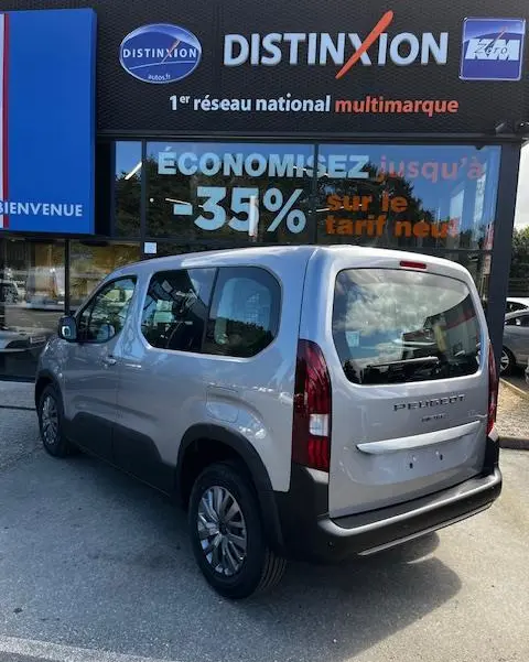 Vue 3/4 arrière droite d’un Peugeot Rifter gris foncé 2024 stationné devant une vitrine avec enseigne Distinxion.