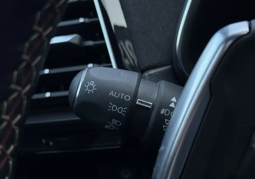 Gros plan sur la commande des phares automatique dans l’habitacle noir du DS7 Crossback blanc, côté gauche du volant.