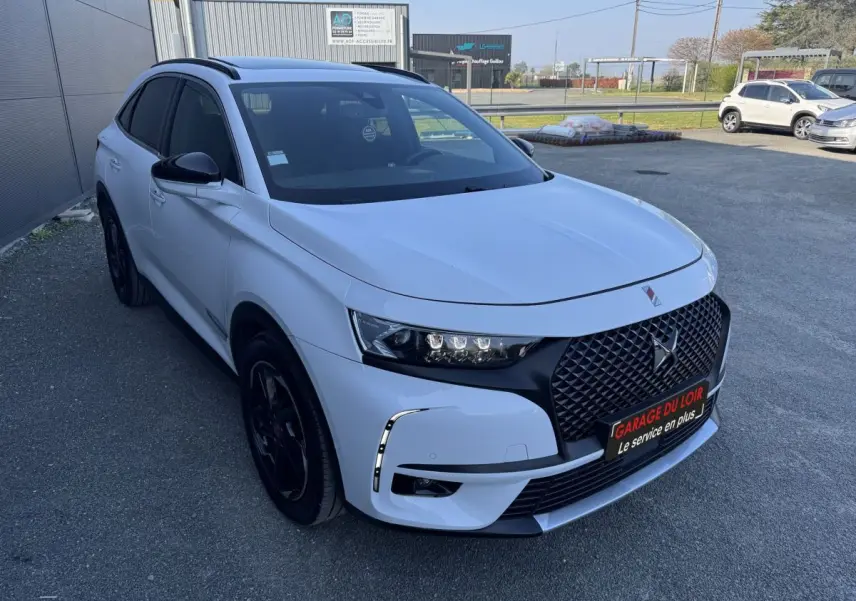DS7 Crossback blanc vue 3/4 avant droit, calandre noire distinctive et phares LED modernes, stationné en extérieur.