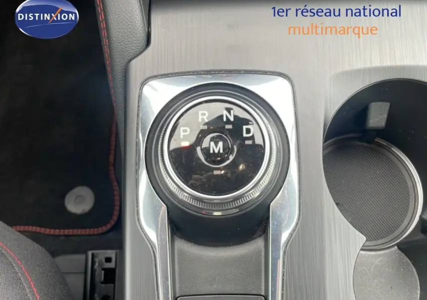 Gros plan sur la molette de boîte automatique du Ford Kuga 2024, avec console grise et surpiqûres rouges visibles.