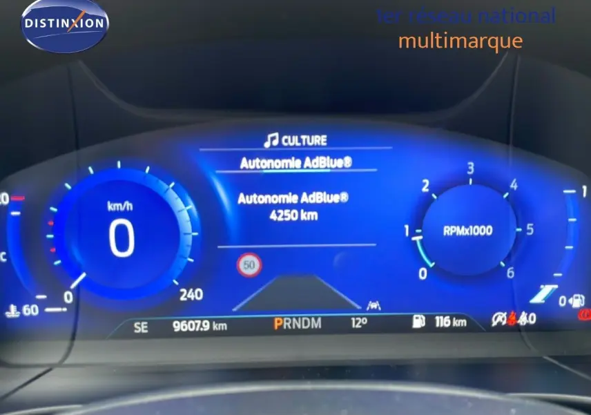 Vue rapprochée du tableau de bord numérique bleu du Ford Kuga 2024 affichant la vitesse, le régime et l'autonomie AdBlue.