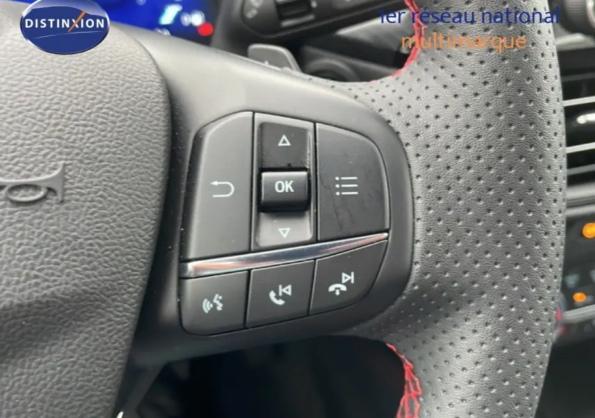 Gros plan sur le volant en cuir noir perforé avec surpiqûres rouges du Ford Kuga 2024, boutons de commande visibles.