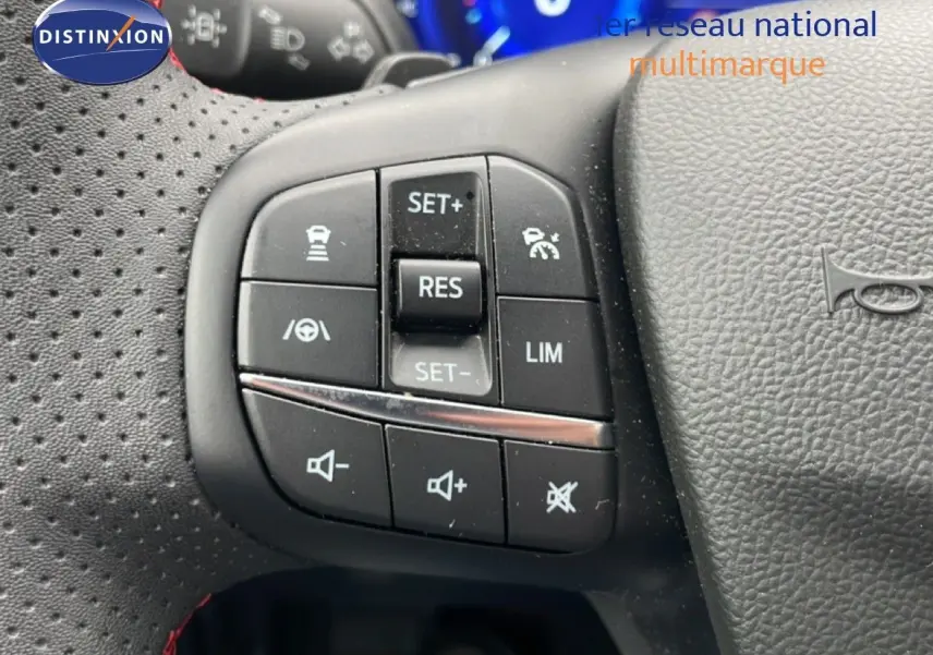 Gros plan sur les commandes au volant côté gauche du Ford Kuga bleu chrome 2024, avec boutons de régulateur et volume sonore.