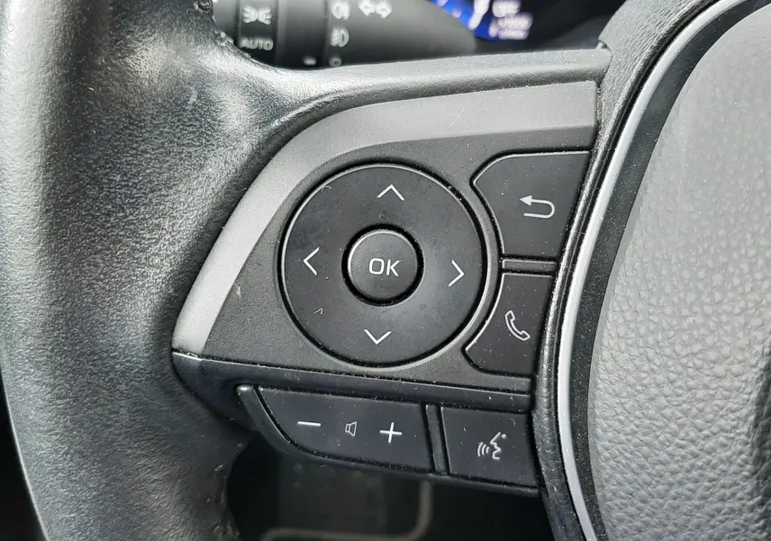 Gros plan sur les commandes multifonctions côté gauche du volant noir d'une Toyota Corolla blanche hybride 2022.