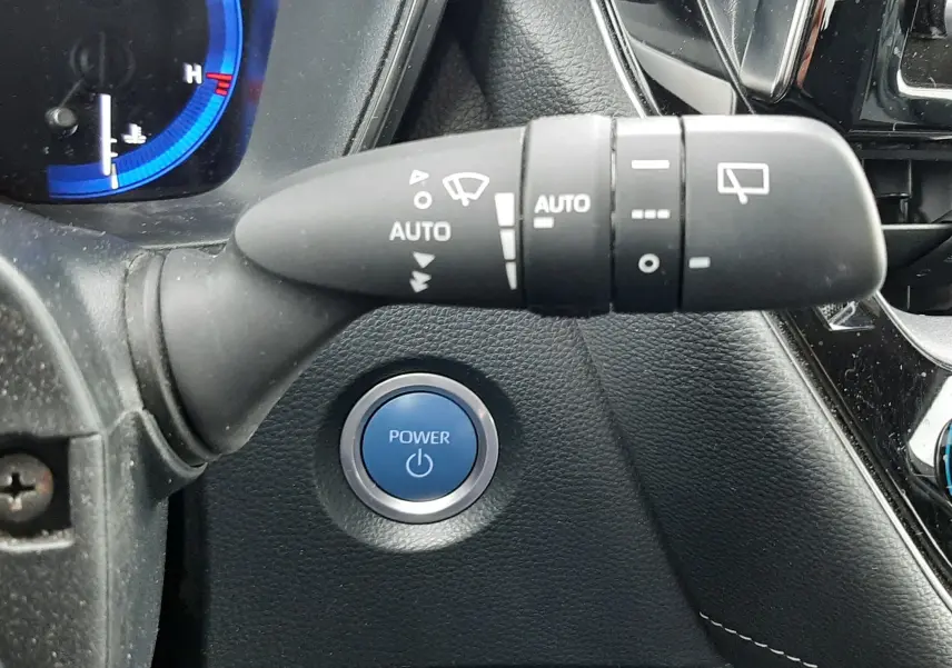 Gros plan sur la commande d'essuie-glace et le bouton start bleu dans l'habitacle noir de la Toyota Corolla blanche 2022.
