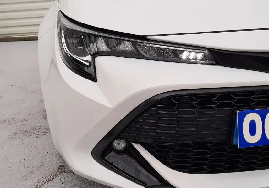 Gros plan sur l'avant droit blanc d'une Toyota Corolla 122 CH Dynamic 2022, mettant en valeur le phare LED et la calandre noire.