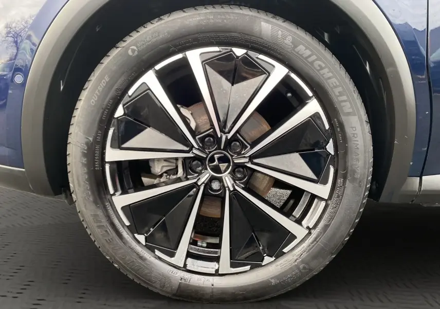 Gros plan sur la roue avant droite du DS7 Bleu Éclipse, mettant en valeur la jante alliage noire et argentée au design géométrique.