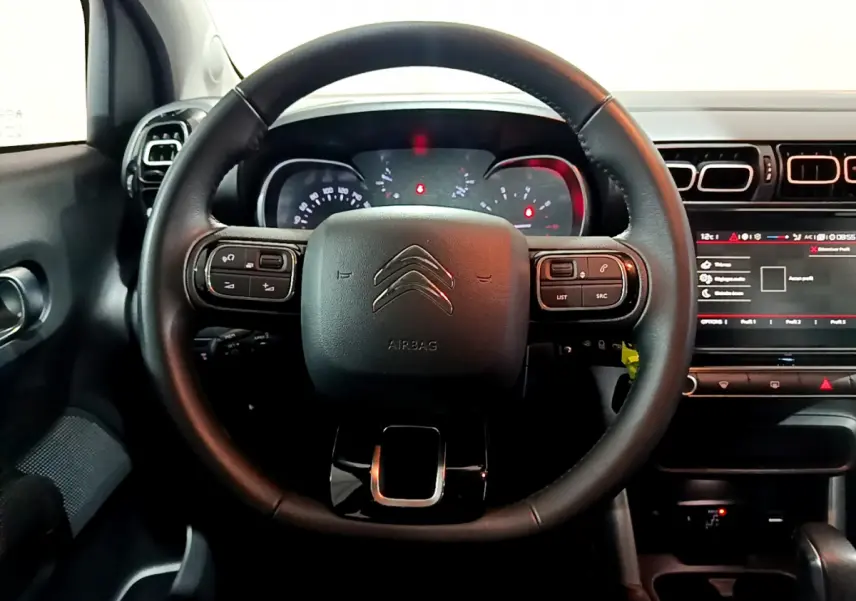 Vue rapprochée du volant cuir noir du Citroën C3 Aircross 2019 avec commandes intégrées et tableau de bord éclairé.