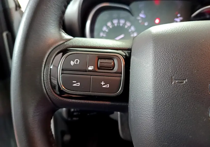 Gros plan sur le côté gauche du volant cuir noir du Citroën C3 Aircross blanc, avec commandes audio intégrées.