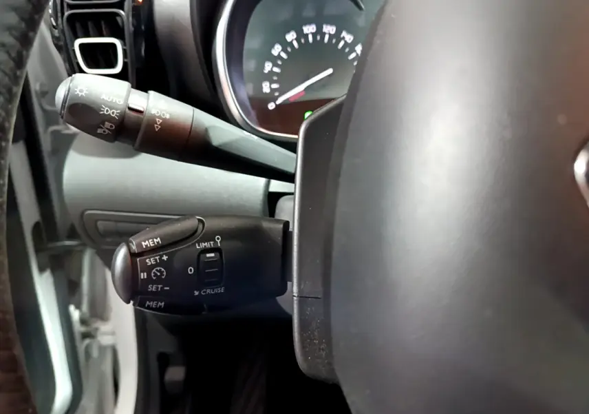 Gros plan sur la commande de régulateur de vitesse à gauche du volant cuir d'une Citroën C3 Aircross blanche de 2019.