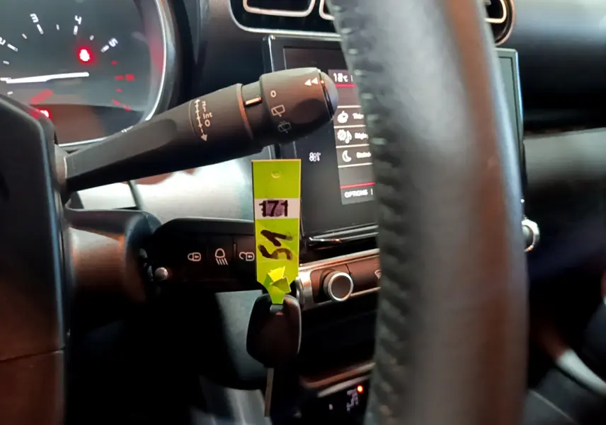 Gros plan sur la colonne de direction et le volant cuir noir d'une Citroën C3 Aircross blanche, tableau de bord en arrière-plan.