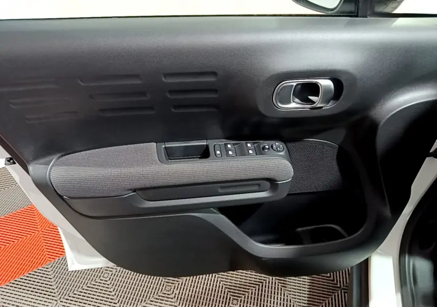 Vue rapprochée de la porte avant gauche noire et grise du Citroën C3 Aircross blanc, avec commandes électriques et poignée chromée.