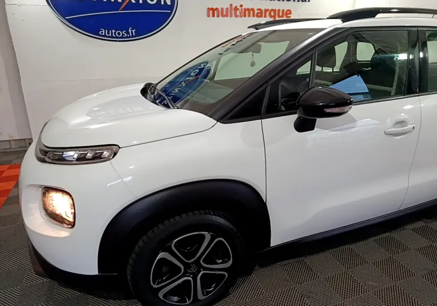 Vue de profil avant droit d'un Citroën C3 Aircross blanc avec feux allumés et rétroviseur noir brillant.