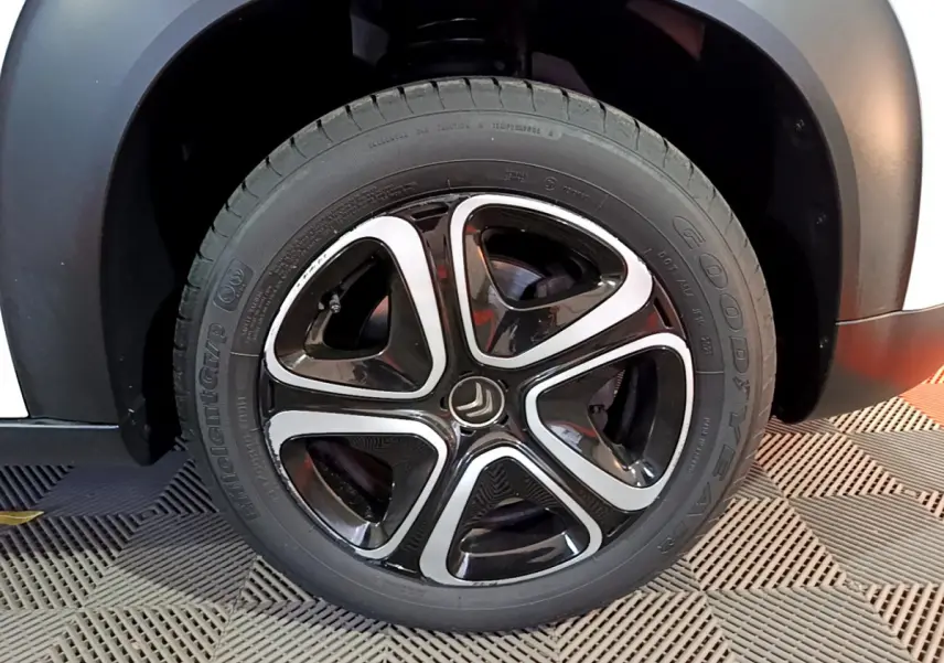 Gros plan sur la roue avant droite d'une Citroën C3 Aircross blanche, jante alliage noire et argentée au design moderne.
