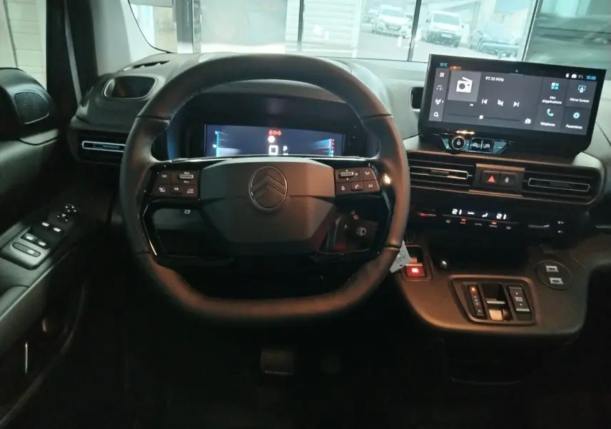 Vue intérieure centrée sur le volant et le tableau de bord numérique du Citroën Berlingo 2025 avec écran tactile et commandes intégrées.