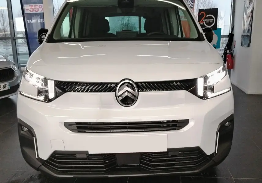 Vue avant d'un Citroën Berlingo blanc 2025 avec calandre noire et phares LED allumés en intérieur showroom.