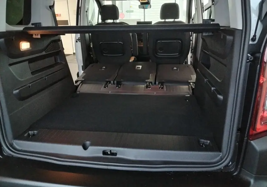 Vue arrière du coffre ouvert du Citroën Berlingo blanc 2025 avec sièges arrière rabattus et cloison amovible.