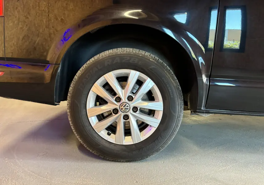 Gros plan sur la roue avant gauche d’un Volkswagen Multivan noir T6 PH.1, soulignant la jante alliage et la carrosserie brillante.