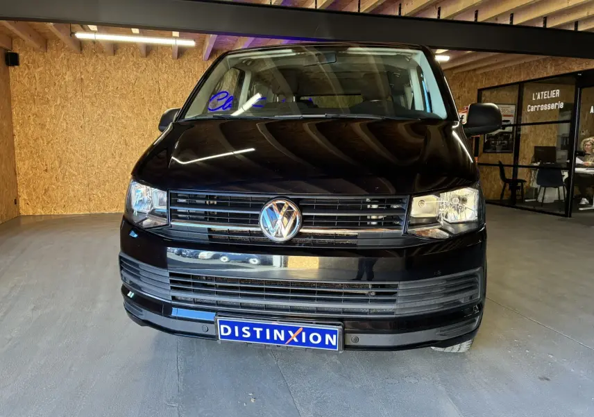 Vue frontale d'un Volkswagen Multivan T6 noir, avec calandre noire et logo VW bien visible, dans un garage.