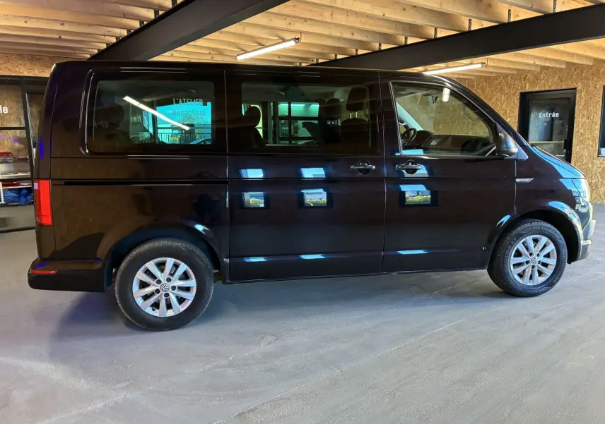 Vue de profil côté gauche d’un Volkswagen Multivan T6 noir, stationné en intérieur avec jantes alliage visibles.