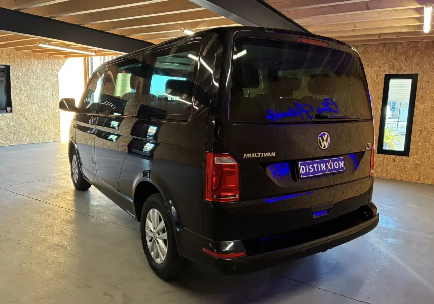 Volkswagen Multivan T6 noir vu en 3/4 arrière droit dans un garage avec reflets bleutés sur la carrosserie.