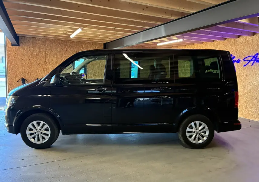Vue de profil côté gauche d’un Volkswagen Multivan T6 noir de 2015 stationné en intérieur avec jantes alliage visibles.