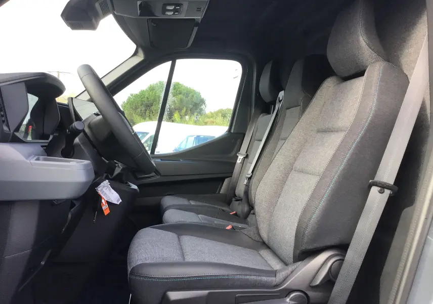 Vue intérieure côté gauche du poste de conduite du Renault Master gris urbain 2025, avec sièges tissu gris et coutures bleues.