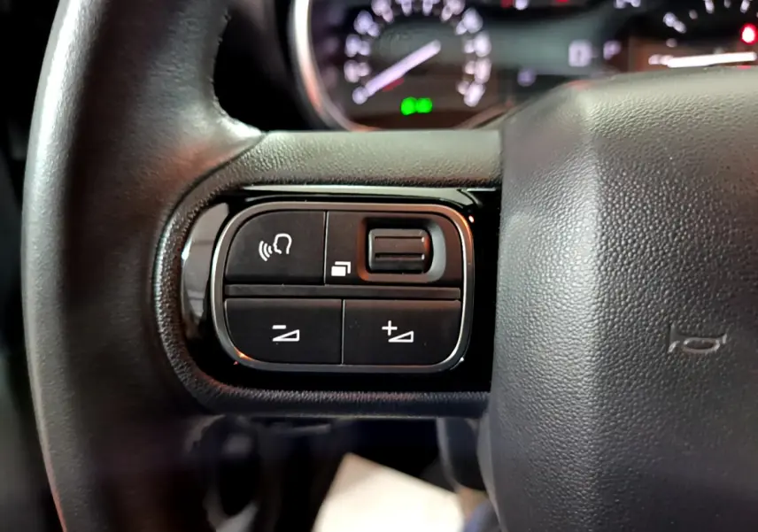 Gros plan sur les commandes gauche du volant cuir noir du Citroën C3 Aircross 2019, avec tableau de bord flou en arrière-plan.