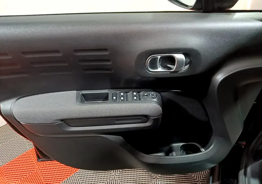Intérieur côté gauche de la porte d'une Citroën C3 Aircross noire, avec commandes de vitres et poignée argentée.