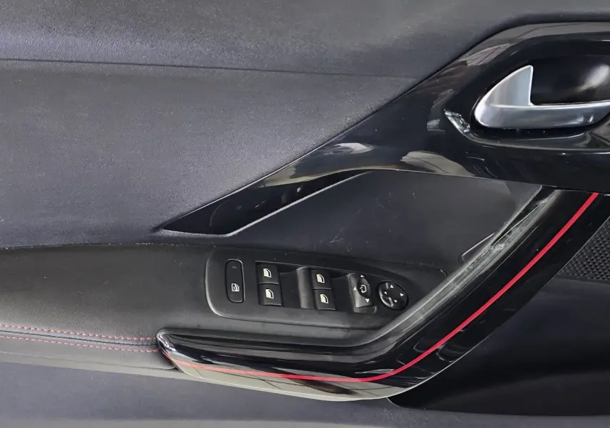 Gros plan sur la porte intérieure côté conducteur de la Peugeot 208 GT-LINE noire avec surpiqûres rouges et commandes électriques.