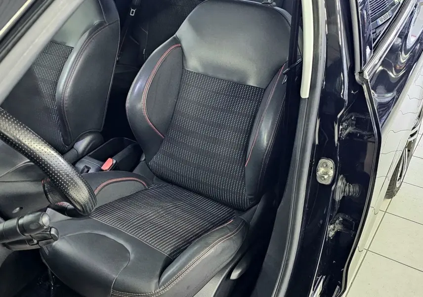 Vue intérieure côté conducteur d'une Peugeot 208 GT-LINE noire de 2015, siège en cuir et tissu avec surpiqûres rouges.