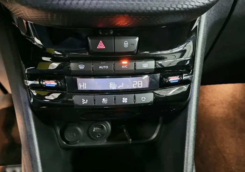 Gros plan sur la console centrale noire de la Peugeot 208 GT-LINE avec commandes de climatisation automatique et prise 12V.
