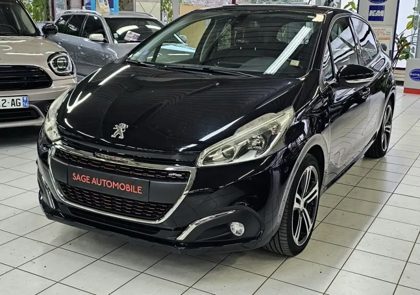 Peugeot 208 GT-LINE noire vue 3/4 avant en intérieur, avec jantes alliage et calandre chromée.