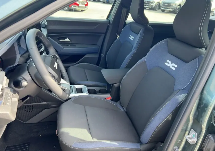 Intérieur avant du Dacia Bigster vert cèdre, sièges tissu noir et bleu avec logo DC, volant cuir visible côté gauche.