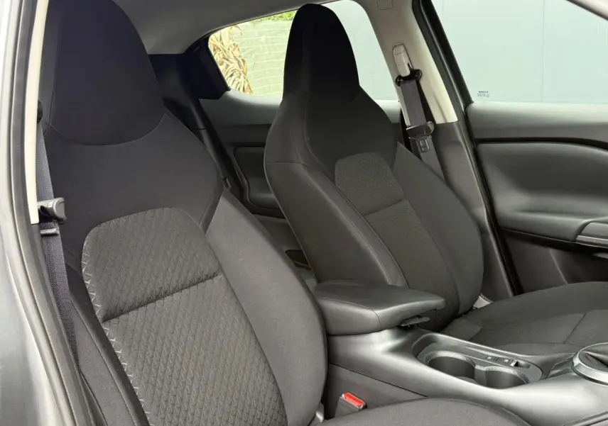 Vue intérieure rapprochée des sièges avant noirs du Nissan Juke 2025, avec accoudoir central et ceintures visibles.