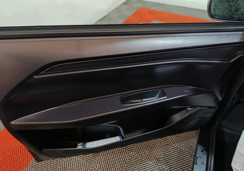 Vue intérieure sur la porte côté conducteur d'une Aixam Ambition gris clair, avec poignée et rangement bas visible.