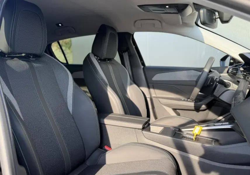Vue intérieure côté conducteur de la Peugeot 308 2025, sièges tissu et cuir noirs avec accoudoir central.