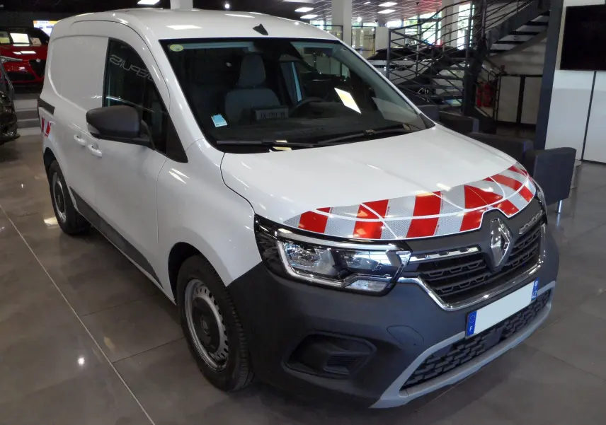 Renault Kangoo Van blanc minéral en 3/4 avant droit avec bandes réfléchissantes rouges sur le capot, en intérieur showroom.
