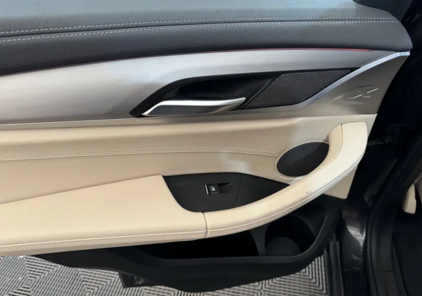 Gros plan sur la porte côté gauche d'une BMW X3 gris foncé, avec garniture beige et insert aluminium marqué "X".